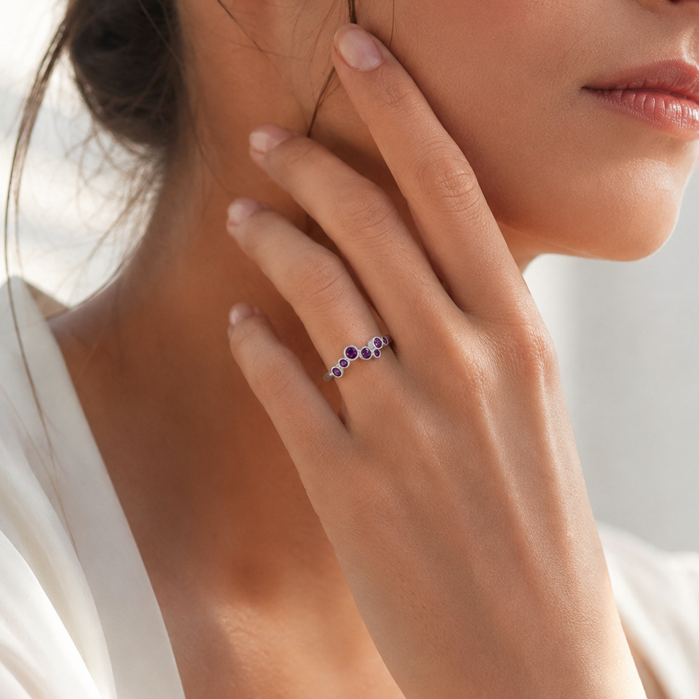 Woman wearing a ring with a small purple gemstone, touching her face.
